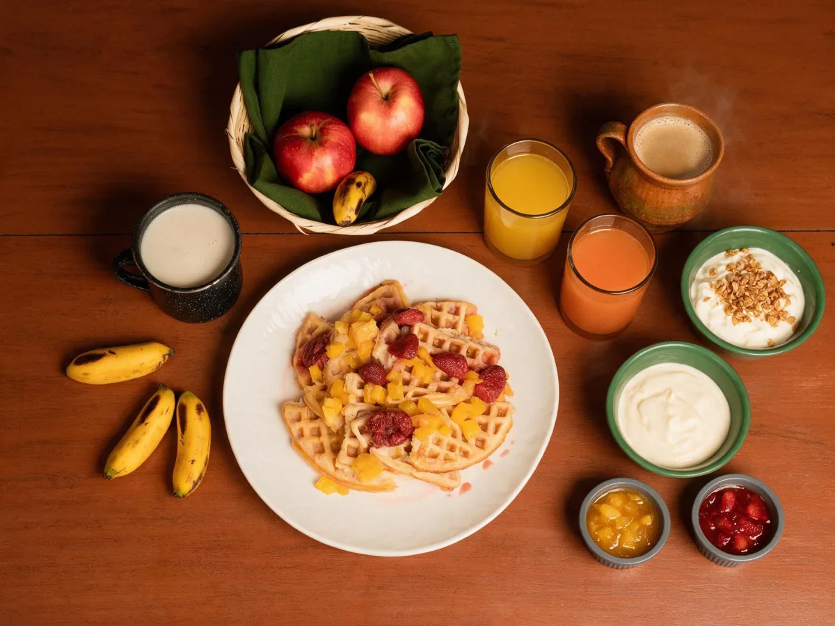 Waffles, fruta, yogurt, granola, café y mermeladas sobre una mesa de desayuno
